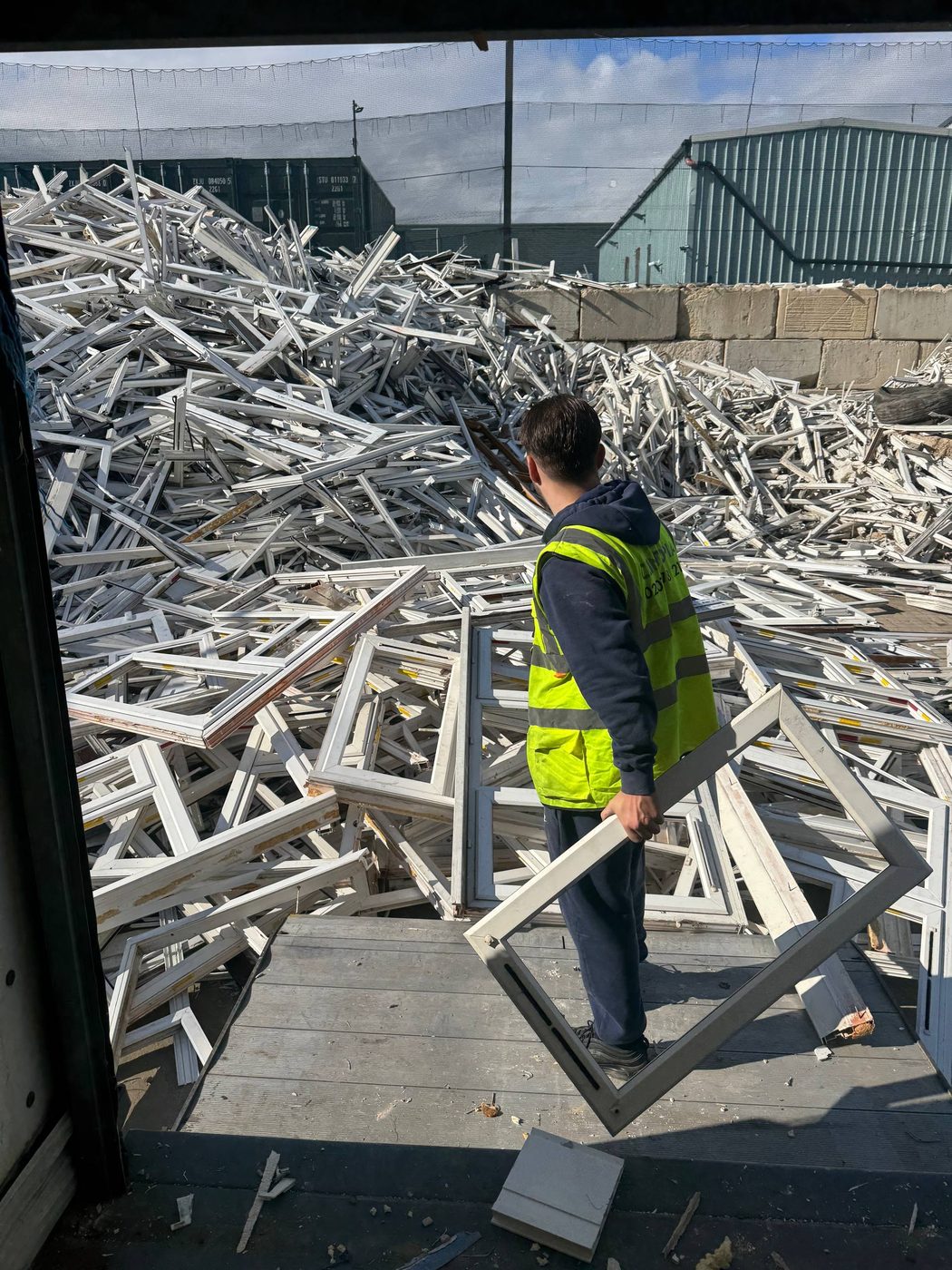 Worker handling a window frame beside a large uPVC frame pile